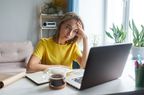 woman in yellow shirt sitting in front of laptop and coffee mug experiencing head pain 