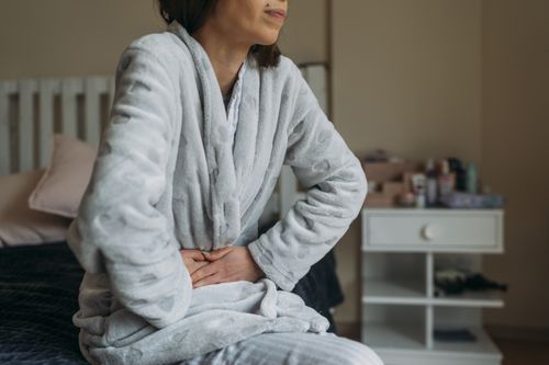 woman sitting in robe experiencing abdominal pain