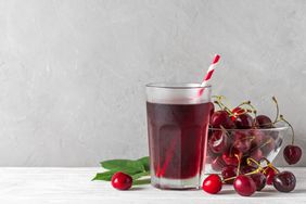 glass of cherry juice and bowl of cherries in front of blank white background