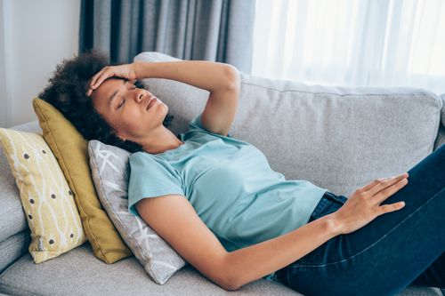 woman lying on a sofa holding her head