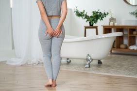 White woman with her hands on her clothed bottom walking toward a bathtub