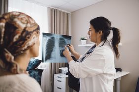 Hispanic female expertise giving advice to cancer patient while examining x-ray at doctor's office