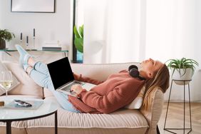 Top view above of a young casual woman in headphones sleeping with gadgets in their hands on cozy sofa in living room keeping eyes closed