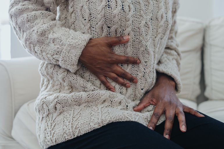 Black woman with hand on stomach wearing white sweater