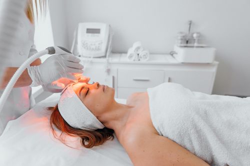 Woman in a dermatology office receiving red light therapy from medical professional. 