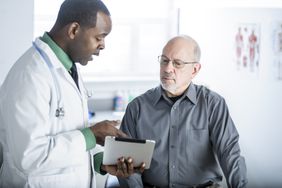 Middle-aged male patient talking to a doctor who is holding a tablet. 