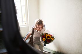 older woman hurrying up stairs with flower in hand