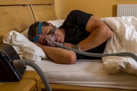 A man sleeps in a bed wearing a mask hooked up to a BiPAP machine 