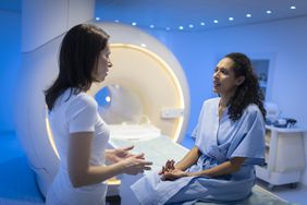 Patient in hospital gown sitting on MRI table talking to doctor