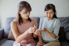 Woman helping her mother check blood sugar level at home