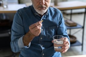 senior man holding glass of water taking medicine