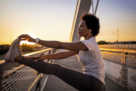 Young African American woman jogging across the bridge at sunset
