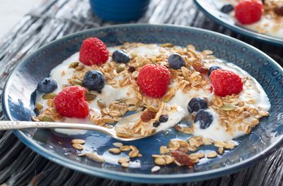 Breakfast of yogurt topped with granola, blueberries, raspberries and maple syrup served on a plate