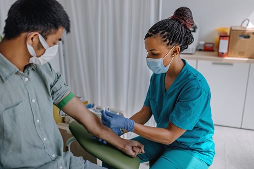 A healthcare worker prepares to take blood from a patient's arm