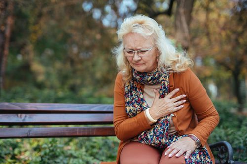woman sitting on park bench holding her heart with chest pain 