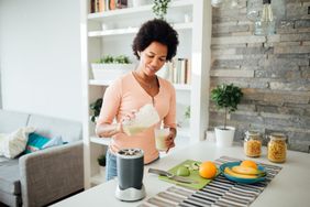 An African American woman making a protein smoothie in the kitchen.