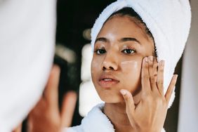 woman with towel applying cream on face