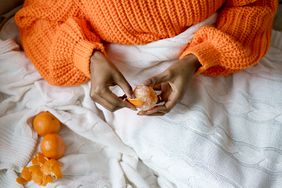 Woman Hands Peeling Ripe Sweet Tangerine Wearing Orange Sweater Lying In Bed Under The Blanket